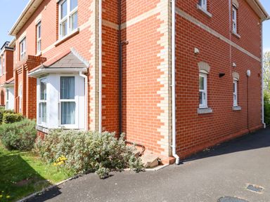 A corner view of a red brick house with white-framed windows and shrubs along the side at Marina Reach in Weymouth