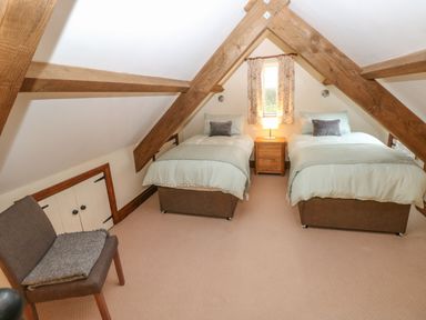 A bedroom with two single beds a nightstand and a chair under a sloped ceiling with wooden beams at The Old Dairy in Maenclochog