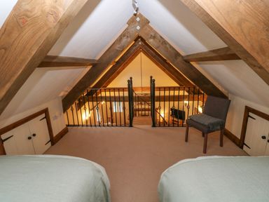 An attic bedroom with two beds a chair small doors and wooden beams at The Old Dairy in Maenclochog