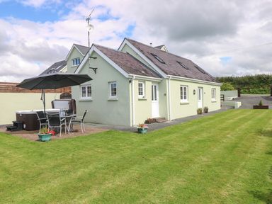 A house with a patio table set and umbrella on a paved area next to a lawn at The Old Dairy in Maenclochog