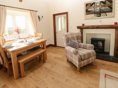 A dining area with a wooden table set for four and a plaid armchair near a fireplace at The Old Dairy in Maenclochog