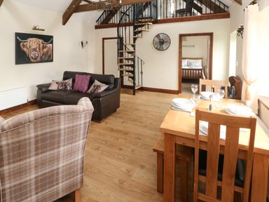 A living room with a dining table set for four and a spiral staircase at The Old Dairy in Maenclochog