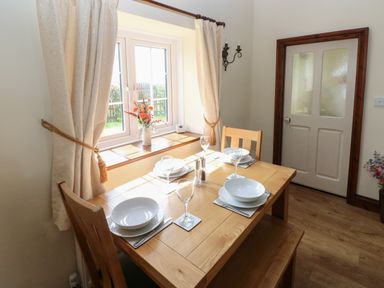 A dining room with a wooden table set for four by a window with curtains at The Old Dairy in Maenclochog