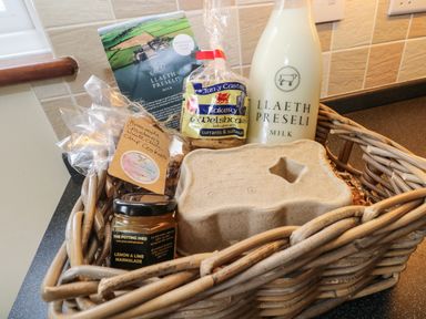 A wicker basket with a bottle of milk, a jar of lemon and lime marmalade, a pack of Welshcakes, a pack of homemade cookies, and a paper carton at The Old Dairy in Maenclochog