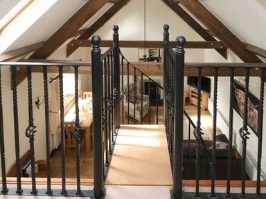 An interior view of a room with a black metal railing bridge leading to a wooden floor with a plaid armchair a wooden dining table with chairs and a television on a wooden stand at The Old Dairy in Maenclochog