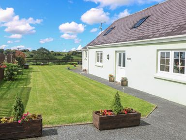 A house with a white exterior and a lawn with flowerpots and a wooden fence at The Old Dairy in Maenclochog