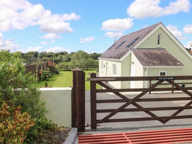A driveway with a wooden gate and a house with skylight windows in the background at The Old Dairy in Maenclochog