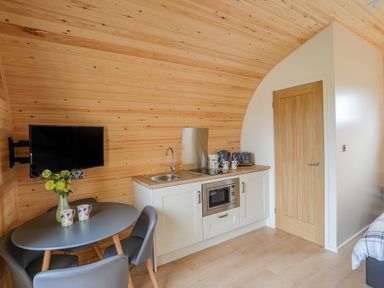 A small kitchen area with a sink microwave and toaster next to a round table with chairs and a wall-mounted TV at Caban Cariad in Bryngwran near Bodedern