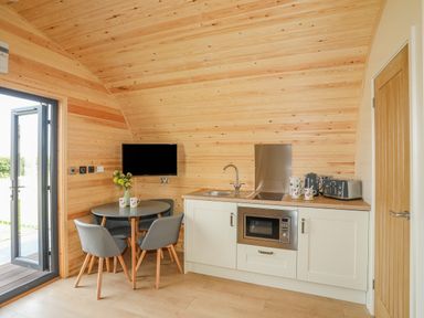 A small kitchen area with a round table and chairs a microwave an electric stove kettle and toaster at Caban Cariad in Bryngwran near Bodedern