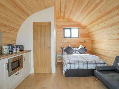A wooden room with a bed towels kitchen appliances and a gray sofa at Caban Cariad in Bryngwran near Bodedern