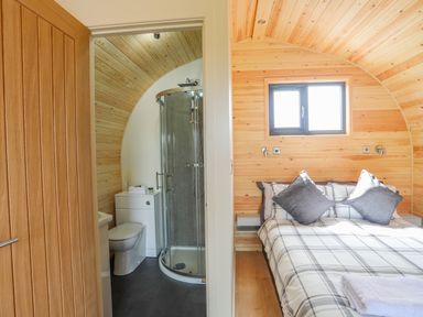 A bedroom with a double bed and plaid bedding next to a bathroom with a curved glass shower at Caban Cariad in Bryngwran near Bodedern