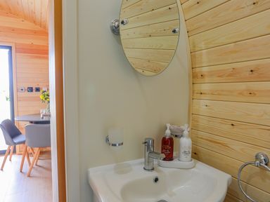 A bathroom sink with soap dispensers and a round mirror next to a dining area with chairs and a table at Caban Cariad in Bryngwran near Bodedern