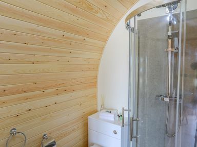 A bathroom with wooden panel walls a glass shower enclosure and a white cabinet with towels at Caban Cariad in Bryngwran near Bodedern
