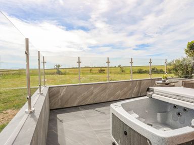 An outdoor patio with a hot tub glass railing and a table with chairs at Caban Cariad in Bryngwran near Bodedern