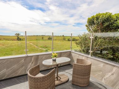 An outdoor patio with a glass table and two wicker chairs overlooking a grassy field at Caban Cariad in Bryngwran near Bodedern