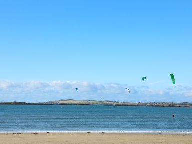 A beach with people kite surfing on the water and land visible in the background at Caban Cariad in Bryngwran near Bodedern
