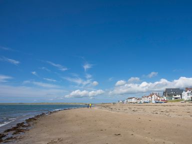 A sandy beach with two people walking near the shore and houses along the beach at Caban Cariad in Bryngwran near Bodedern
