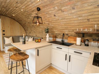 A kitchen area with stools a countertop sink glasses and a seating nook at Tan Y Wawr - Derwen in Llanfair Caereinion