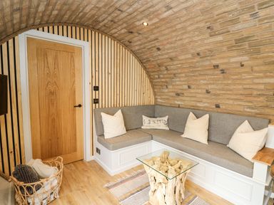A small living area with a built-in gray cushioned corner bench and wooden door under a curved brick ceiling at Tan Y Wawr - Derwen in Llanfair Caereinion