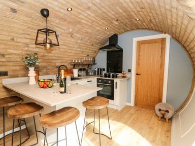 A kitchen with bar stools a wooden door and an arched brick ceiling at Tan Y Wawr - Derwen in Llanfair Caereinion