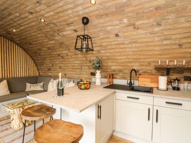 A kitchen with a curved brick wall a countertop with stools a sink and a seating area at Tan Y Wawr - Derwen in Llanfair Caereinion