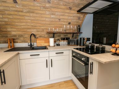 A kitchen corner with a sink stove oven countertop and shelves with glasses at Tan Y Wawr - Derwen in Llanfair Caereinion