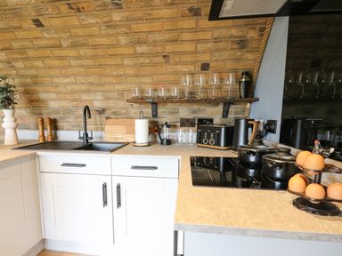 A kitchen countertop with a black sink faucet cutting board toaster kettle and pots at Tan Y Wawr - Derwen in Llanfair Caereinion