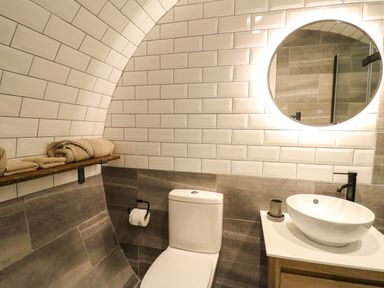 A bathroom with a toilet sink round mirror and towels on a shelf at Tan Y Wawr - Derwen in Llanfair Caereinion