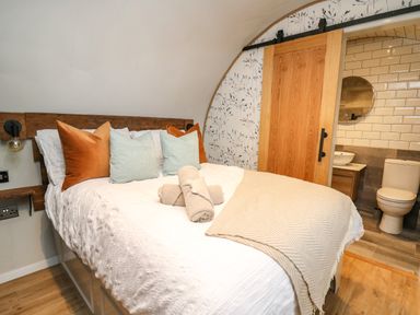 A bedroom with a double bed pillows towels a wooden sliding door and an ensuite bathroom at Tan Y Wawr - Derwen in Llanfair Caereinion