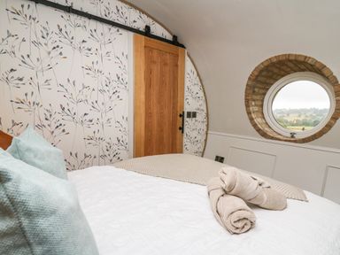 A bedroom with a bed and rolled towels near a round window with a countryside view at Tan Y Wawr - Derwen in Llanfair Caereinion
