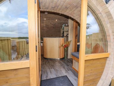 Arched entrance with wooden doors leading to a room with wooden flooring a curved wooden reception desk and a bench with cushions at Tan Y Wawr - Derwen in Llanfair Caereinion