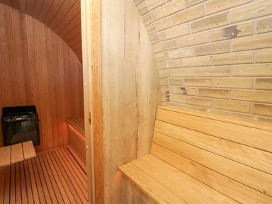 A wooden bench next to a brick wall in a sauna room with wooden paneling and a heater at Tan Y Wawr - Derwen in Llanfair Caereinion