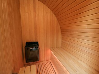 An interior view of a wooden sauna with a bench and a black Harvia heater at Tan Y Wawr - Derwen Llanfair Caereinion
