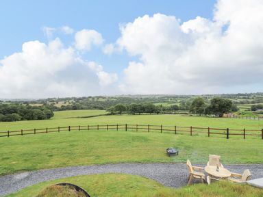 A grassy field with a wooden fence and a seating area with chairs and a table at Tan Y Wawr - Derwen in Llanfair Caereinion