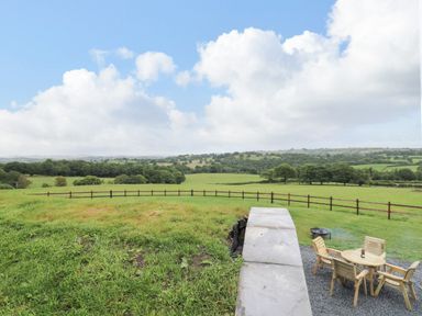 A grassy field with a wooden fence a circular outdoor seating area with chairs and a table at Tan Y Wawr - Derwen in Llanfair Caereinion