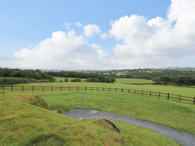 A view of green fields with a wooden fence and distant trees under a partly cloudy sky at Tan Y Wawr - Derwen in Llanfair Caereinion