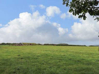A grassy field with a small earth-covered building and fence under a blue sky at Tan Y Wawr - Derwen in Llanfair Caereinion