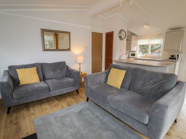 A living room with two grey sofas and yellow cushions next to a kitchen with a countertop at Wayside Lodge in Aston On Clun