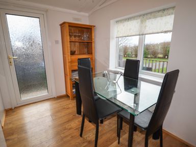 A dining area with glass table four black chairs wooden cabinet and window at Wayside Lodge in Aston On Clun