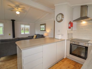 A kitchen with an oven toaster and countertop open to a living room with sofas and windows at Wayside Lodge in Aston On Clun