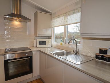 A kitchen with oven, microwave, sink, and window with floral blind at Wayside Lodge in Aston On Clun