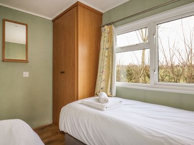 A bedroom with a single bed and towels on it a wooden wardrobe and a window with floral curtains at Wayside Lodge in Aston On Clun