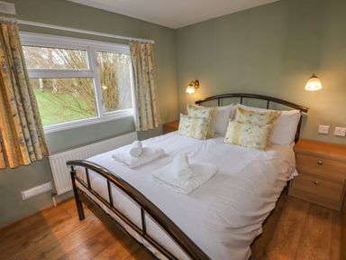 A bedroom with a double bed with white linens and floral pillows and curtains at Wayside Lodge in Aston On Clun