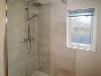 A shower area with glass partition and a window with a blue roller blind at Wayside Lodge in Aston On Clun