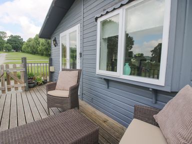 An outdoor wooden deck with wicker chairs and a table outside a blue building at Wayside Lodge in Aston On Clun