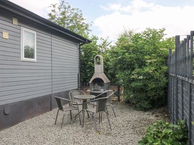 An outdoor seating area with a round table four chairs a built in barbecue grill and a gravel ground at Wayside Lodge in Aston On Clun