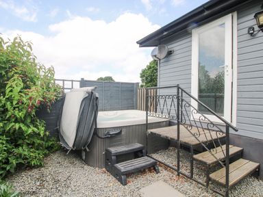 An outdoor hot tub with steps next to a gray building with a door and stairs at Wayside Lodge in Aston On Clun