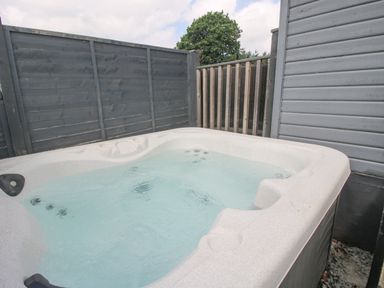 An outdoor hot tub with water in a fenced corner at Wayside Lodge in Aston On Clun