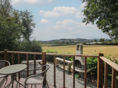 An outdoor patio with a table and chairs overlooking a landscape at Aston - Shepherd Hut Aston On Clun