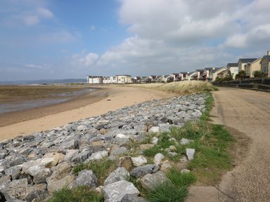 A coastal scene with rocky shoreline sandy beach grass and houses along a road at 5 Pontardulais Road in Llangennech